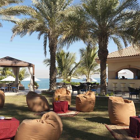 Al Raha Beach Resort & Spa Abu Dabi Restaurante foto The photo depicts a beautiful outdoor setting with several elements of relaxation and leisure. In the foreground, there are large, comfortable bean bag chairs arranged on a grassy area, accompanied by low tables. Surrounding this seating area are tal