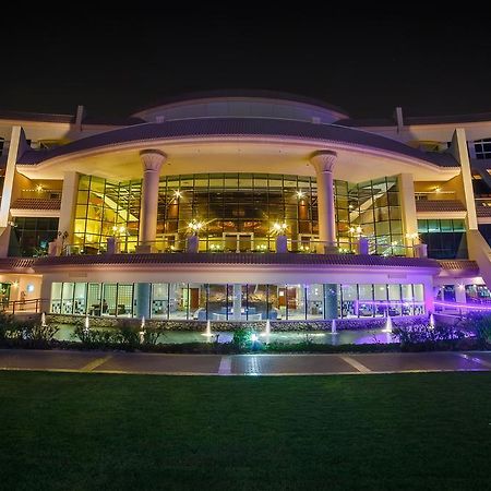Al Raha Beach Resort & Spa Abu Dabi Exterior foto The photo shows a modern architectural building illuminated at night. The structure has a large central entrance with multiple glass windows, flanked by symmetrical columns. The exterior features a combination of sleek lines and curves, with lighting
