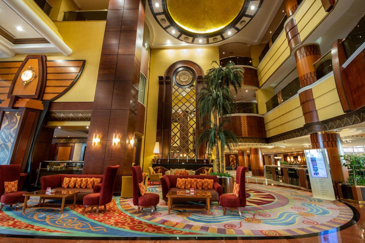 Al Raha Beach Resort & Spa Abu Dabi Exterior foto The photo shows an elegant lobby interior of a hotel. The space features tall ceilings with decorative lighting and large windows, allowing for natural light. There are several plush seating arrangements, including red armchairs and wooden tables, cr