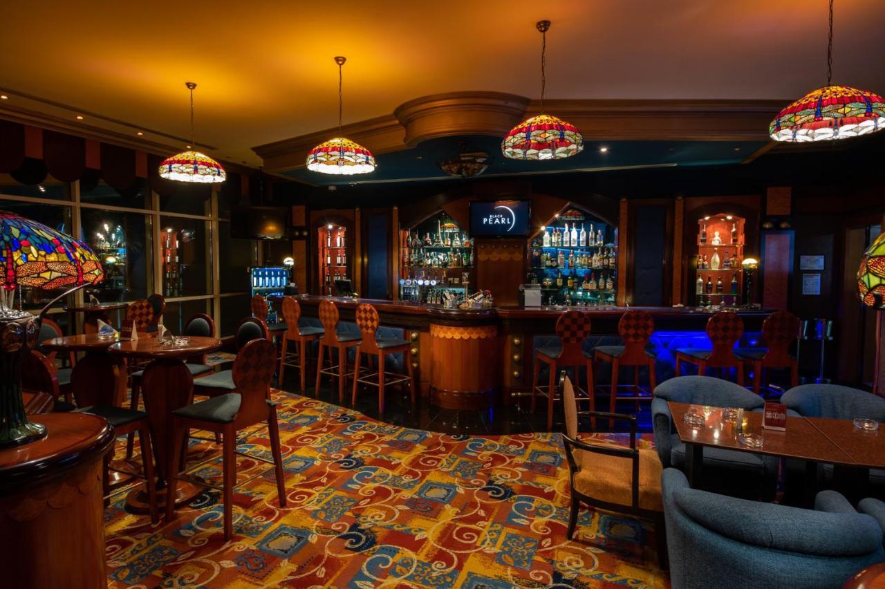 Al Raha Beach Resort & Spa Abu Dabi Exterior foto The photo shows a cozy bar interior, featuring a well-stocked bar area with various bottles displayed on shelves. The bar is illuminated by colorful stained glass light fixtures, creating a warm and inviting atmosphere. The floor is covered with a vi