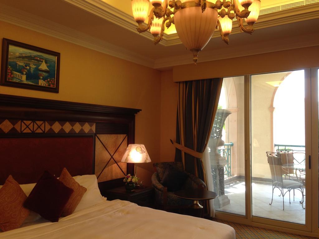 Al Raha Beach Resort & Spa Abu Dabi Exterior foto The photo shows the interior of a hotel room. The room features a large bed with decorative cushions and a wooden headboard. There's a bedside lamp emitting a warm light, and a painting is hung on the wall above the bed. To the right, there's a windo