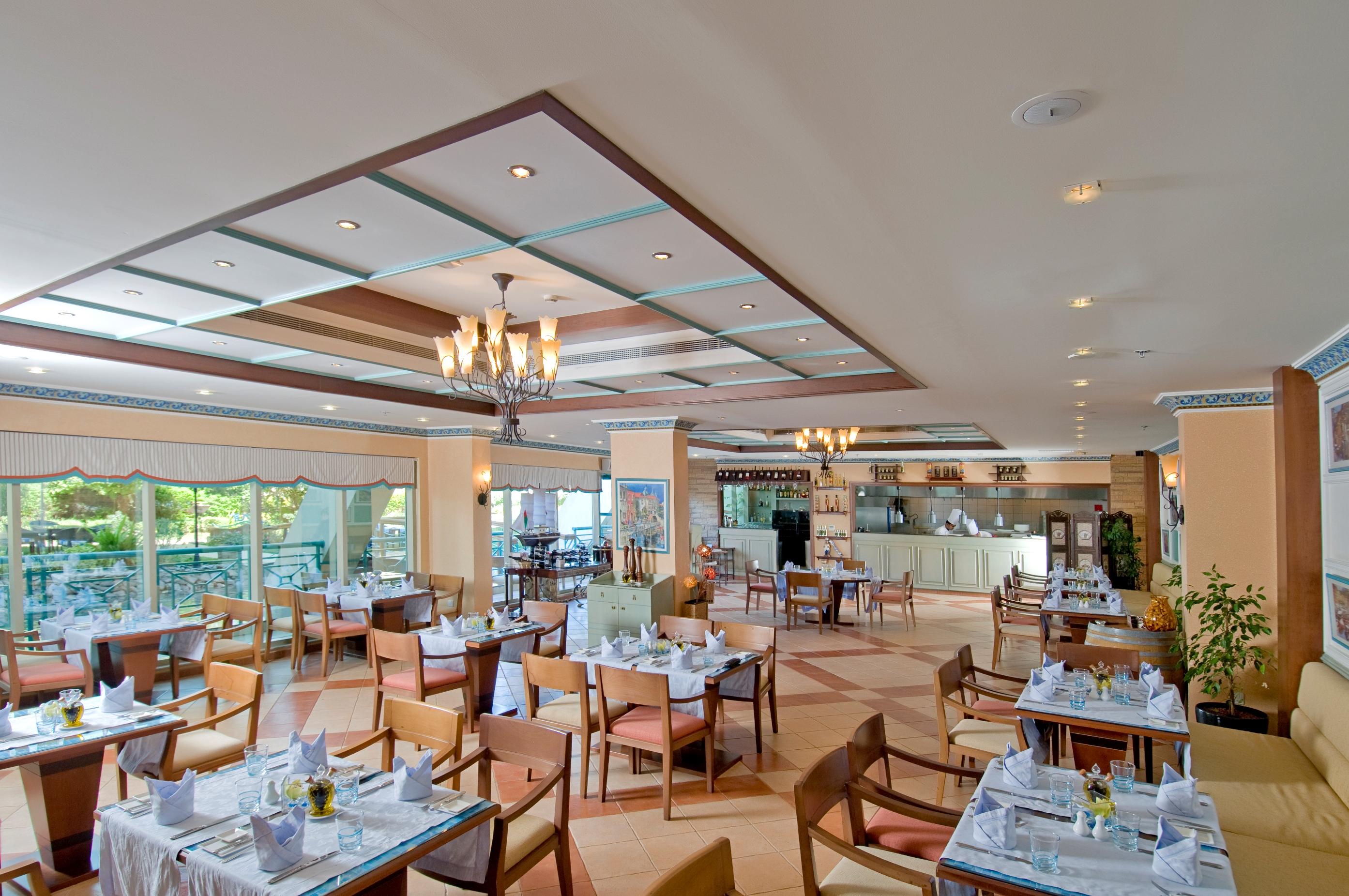 Al Raha Beach Resort & Spa Abu Dabi Restaurante foto The photo shows the interior of a restaurant. It features a spacious dining area with multiple tables neatly arranged, each set with tableware and cloth napkins. The decor includes a decorative ceiling with lighting fixtures, and large windows that p