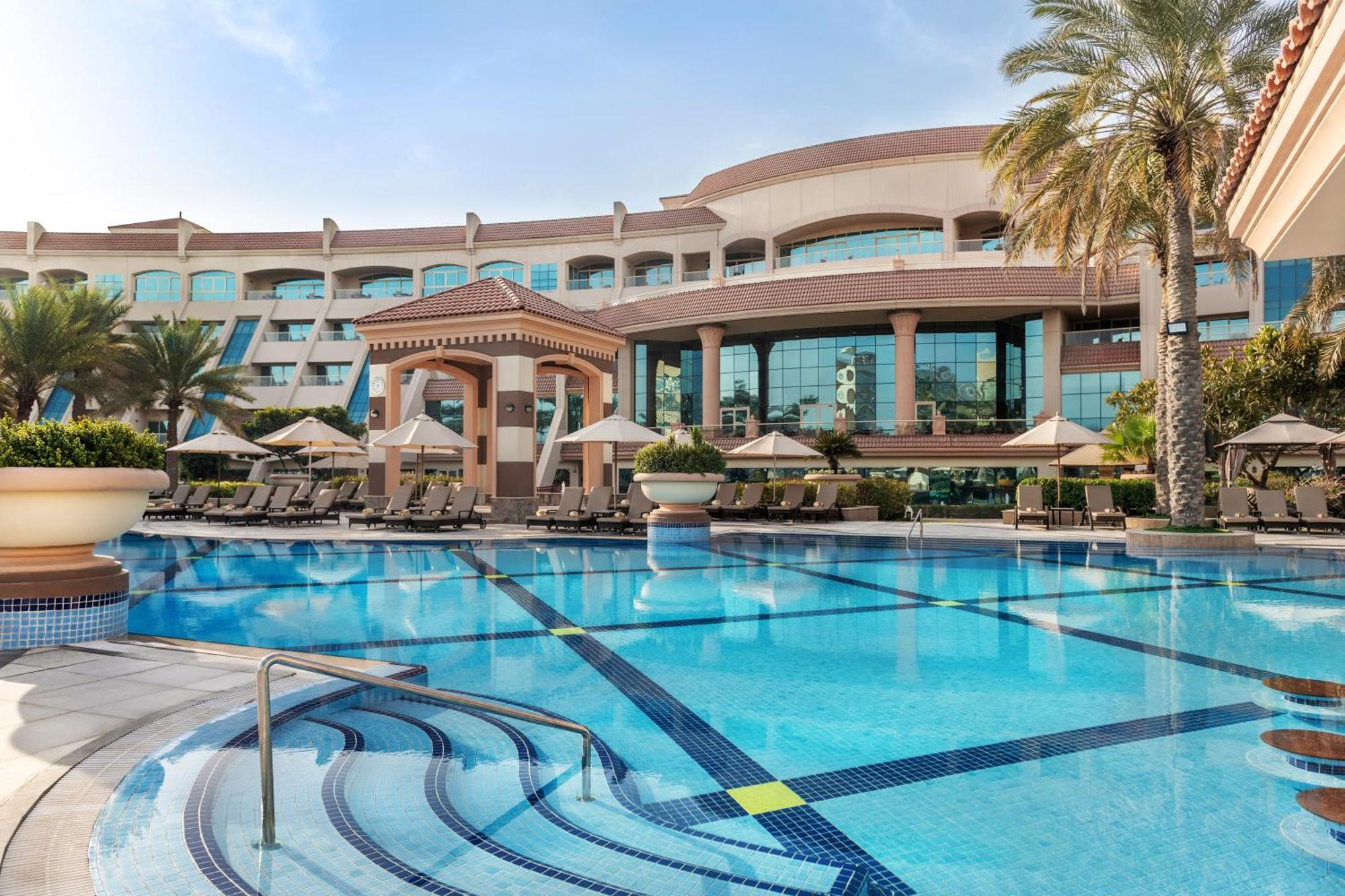 Al Raha Beach Resort & Spa Abu Dabi Exterior foto The photo shows a luxurious resort with a large swimming pool in the foreground. The pool has a clean, blue surface and features lounge chairs on the surrounding deck. In the background, there is a stylish and modern hotel building with multiple stor