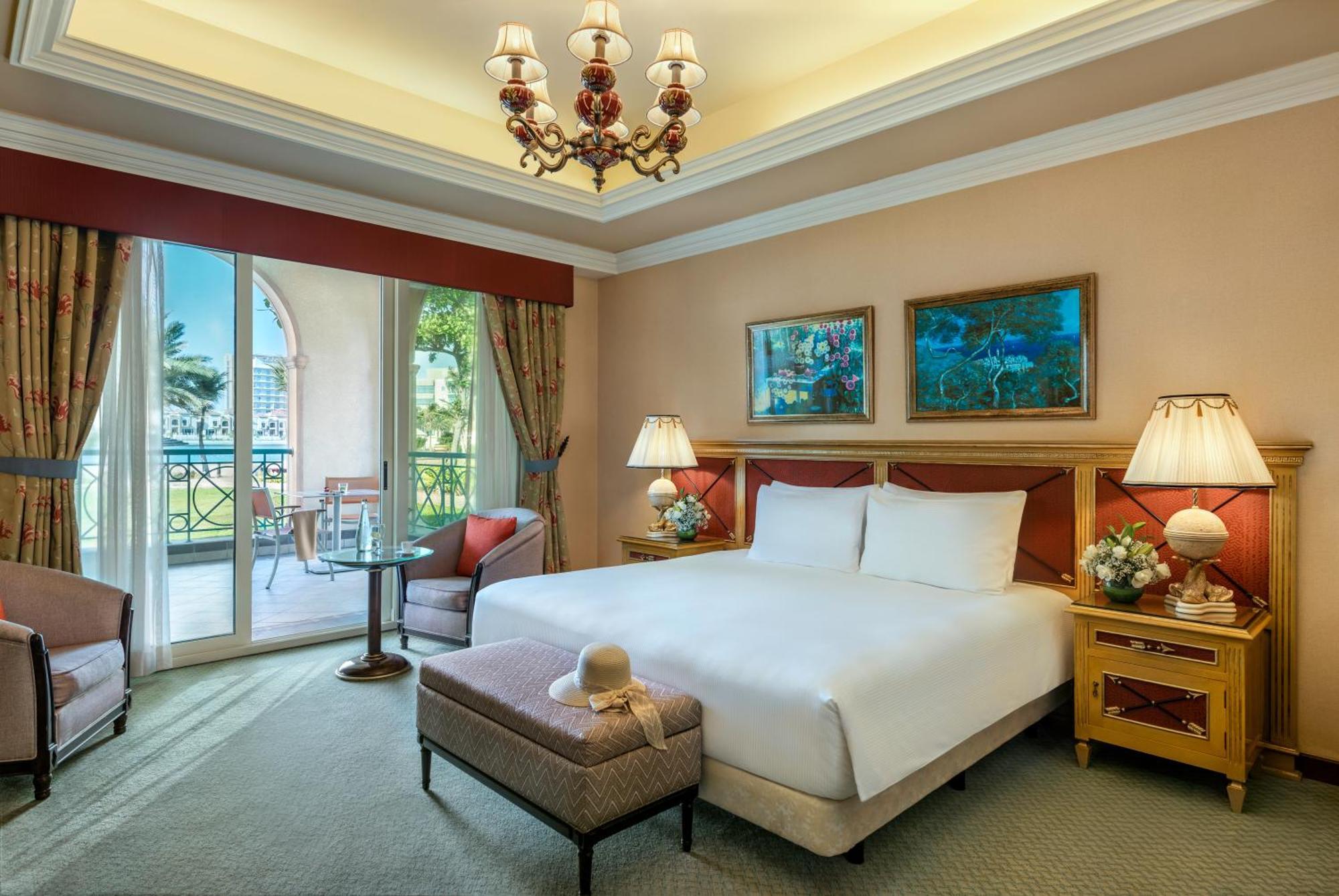 Al Raha Beach Resort & Spa Abu Dabi Exterior foto The image depicts a well-furnished hotel room. It features a large bed with white linens, flanked by two bedside lamps. Above the bed, there are two pieces of artwork hanging on the walls. To the side, there is a comfortable armchair and a small tabl