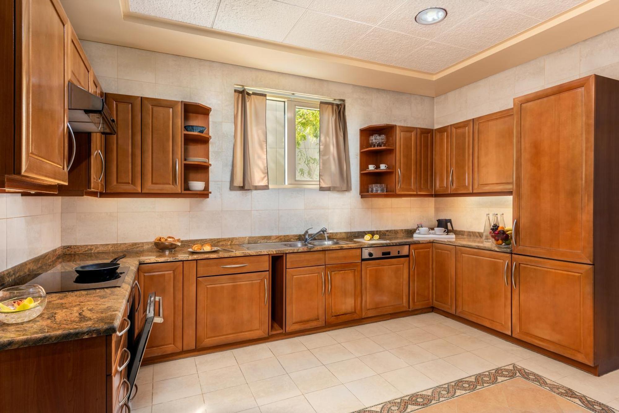 Al Raha Beach Resort & Spa Abu Dabi Exterior foto The photo shows a cozy kitchen featuring wooden cabinets with a rich brown finish, providing a warm and inviting atmosphere. The countertops are made of a light-colored stone, complementing the cabinetry. There is a window above the sink, allowing na