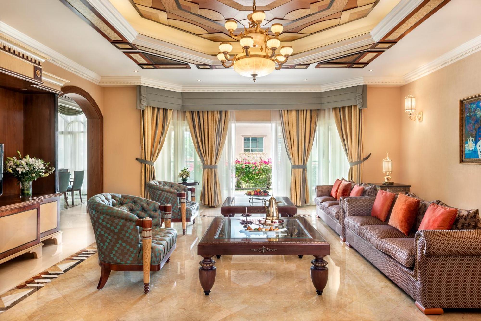 Al Raha Beach Resort & Spa Abu Dabi Exterior foto The photo shows an elegantly designed living room. It features a high, intricately patterned ceiling with a chandelier hanging in the center. The room is filled with natural light from large windows covered with flowing curtains. 

There are two diff
