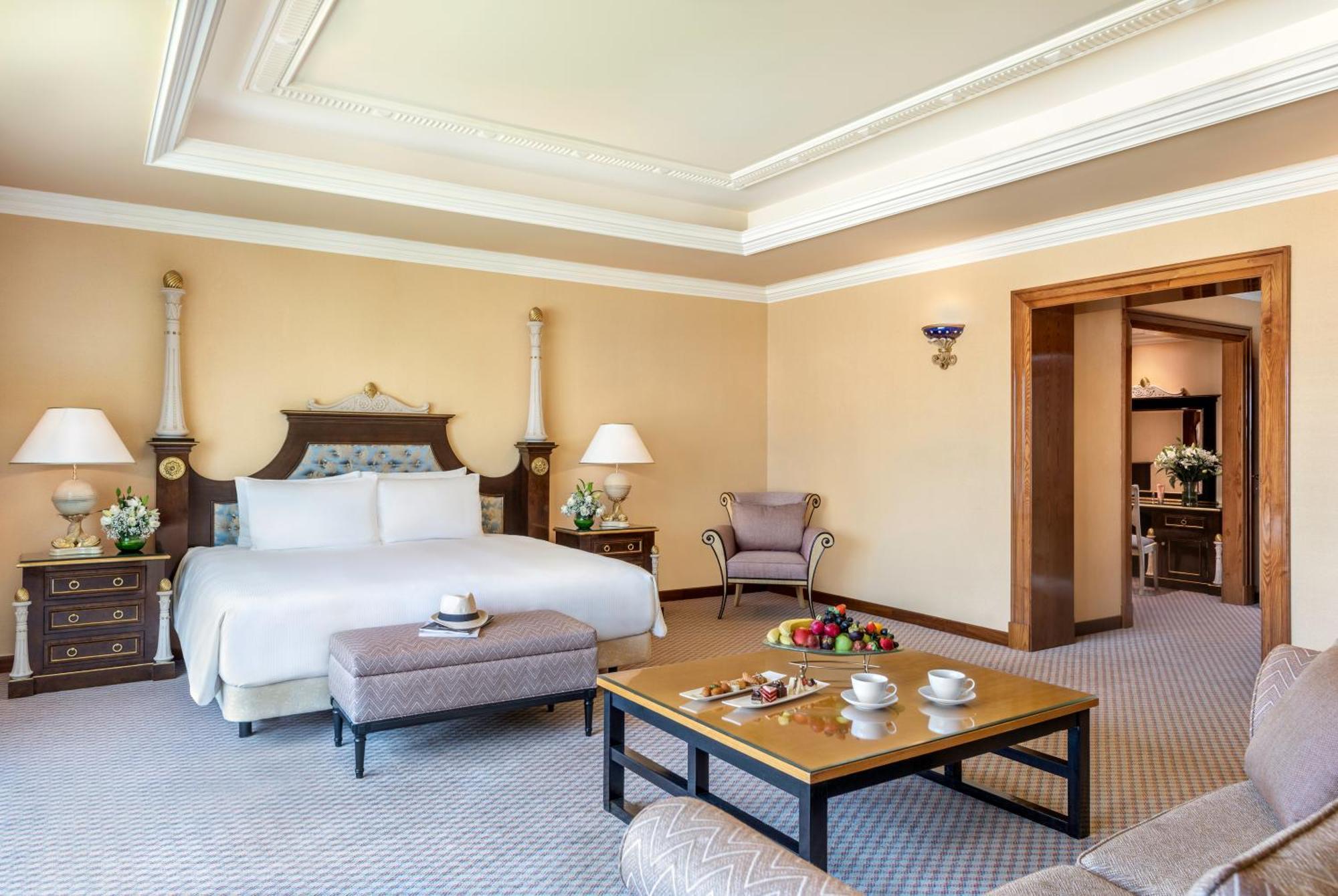 Al Raha Beach Resort & Spa Abu Dabi Exterior foto The photo shows an elegant hotel room, featuring a large bed with white linens, flanked by stylish bedside tables and lamps. The room has a warm color palette, with light brown walls and a plush carpet. A comfortable armchair is positioned nearby, an