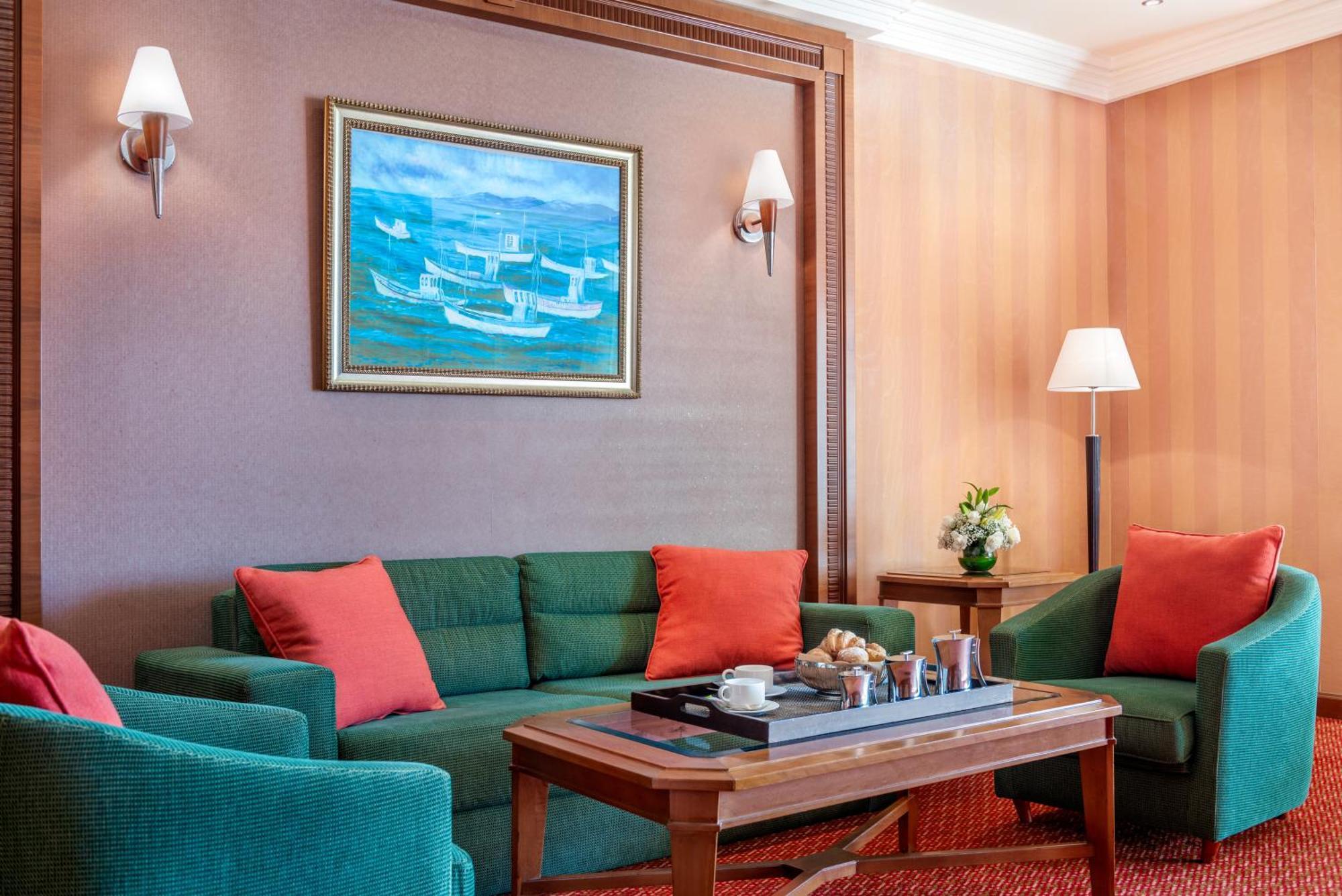 Al Raha Beach Resort & Spa Abu Dabi Exterior foto The photo displays a cozy and elegantly furnished living area. It features a green sofa adorned with orange cushions and two matching green armchairs. A wooden coffee table sits in the center, which holds a tray with beverages and snacks. The walls a