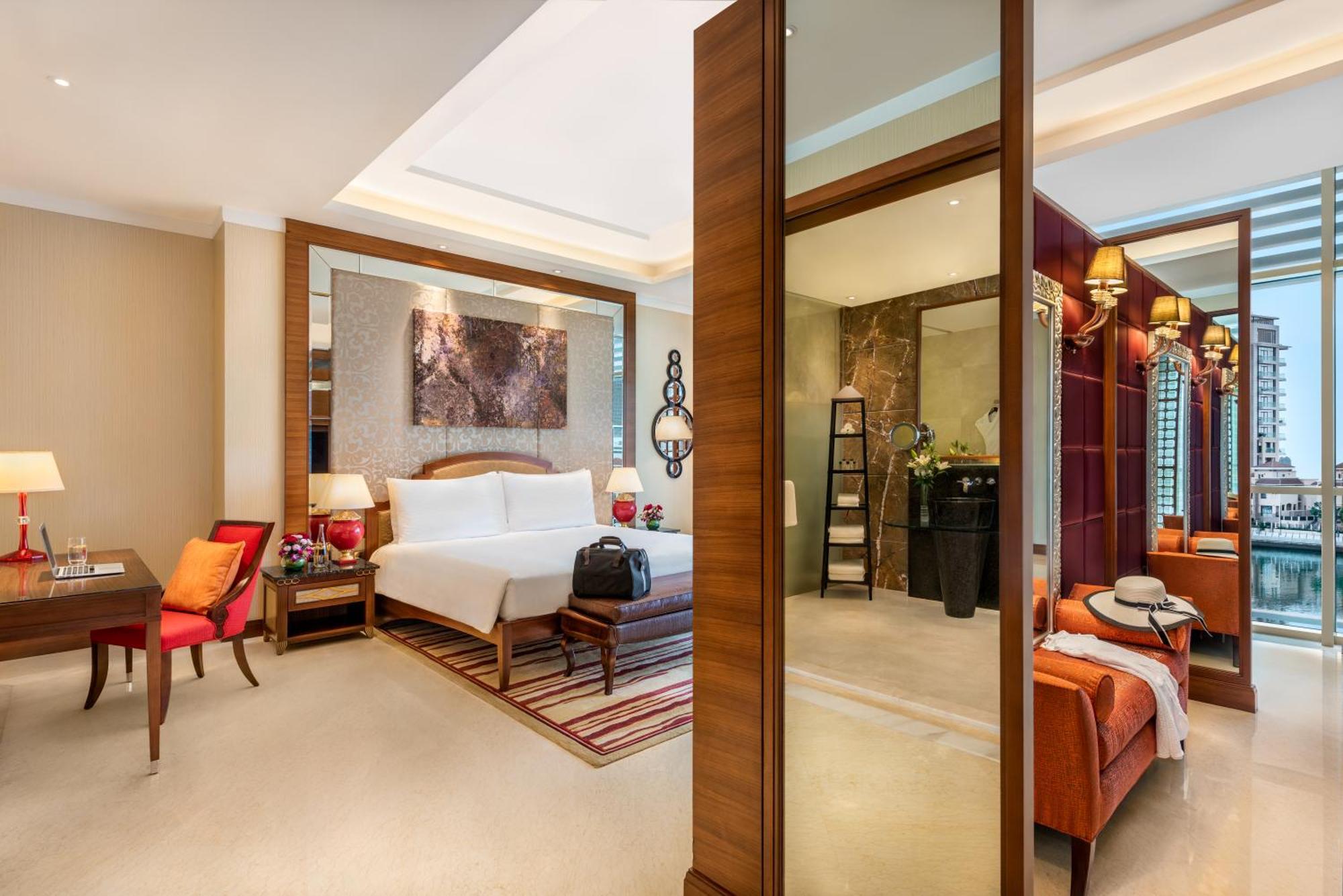 Al Raha Beach Resort & Spa Abu Dabi Exterior foto The photo shows a luxurious hotel room with a modern design. The room features a large bed with white linens, flanked by bedside tables with lamps. There is a area with a chair and a small table on the left side, and a vibrant artwork hanging above t