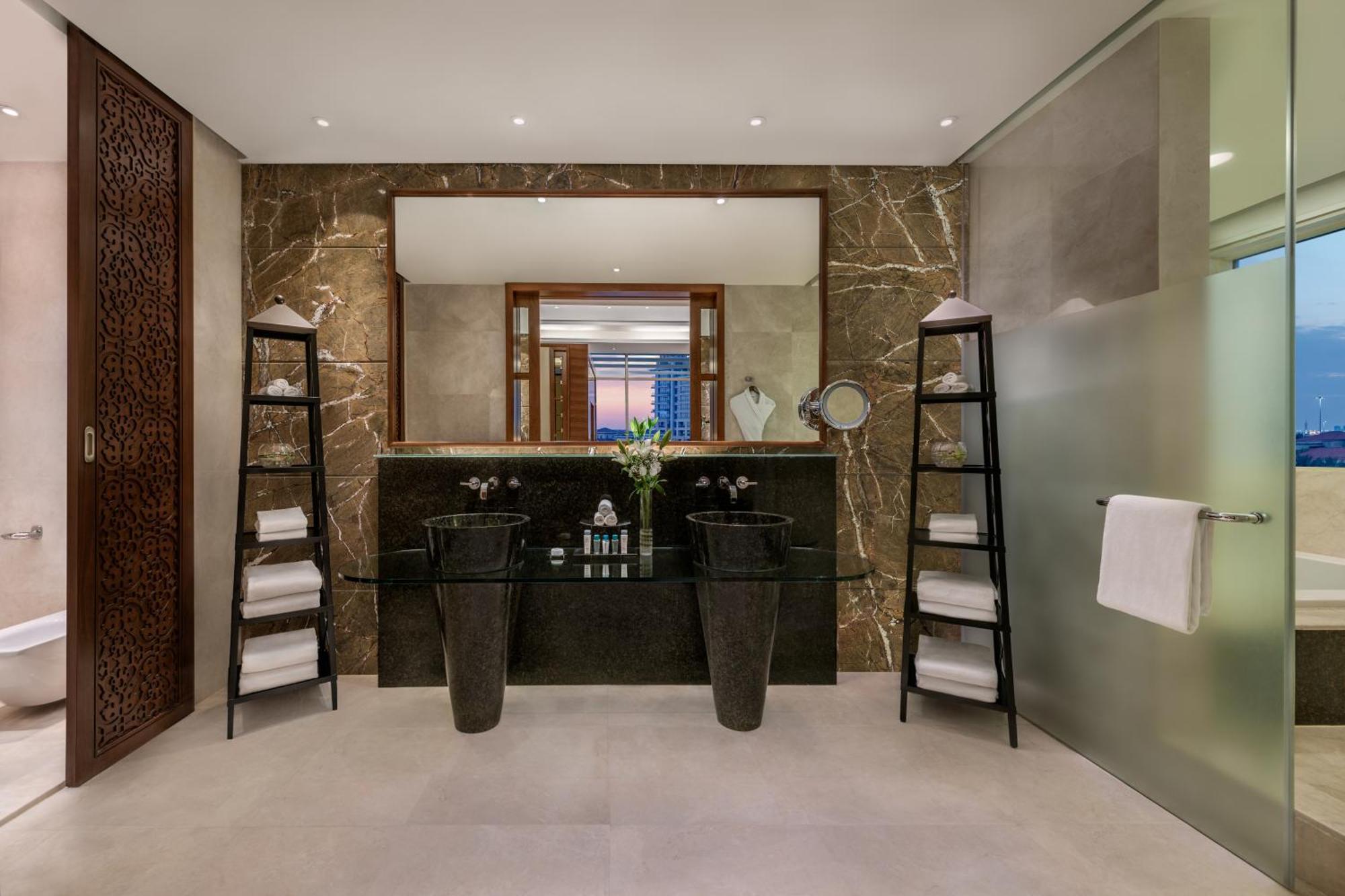 Al Raha Beach Resort & Spa Abu Dabi Exterior foto The photo shows a modern, elegant bathroom interior. It features a large mirror hanging above a double-sink vanity with a dark stone countertop. On either side of the vanity are tall, slender vases that might be holding decorative elements. There are