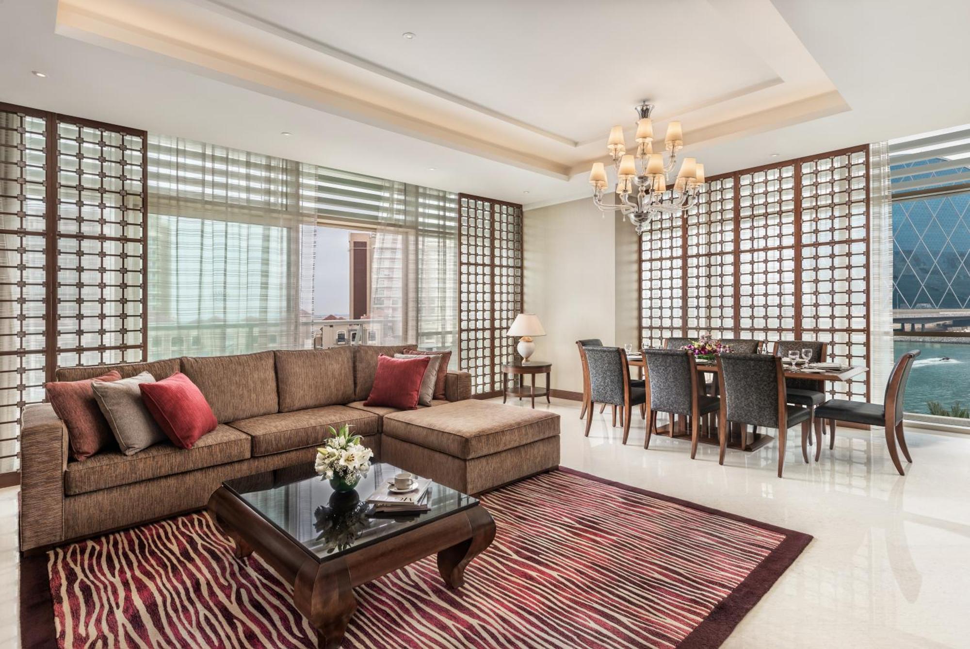 Al Raha Beach Resort & Spa Abu Dabi Exterior foto The photo shows a stylish and modern living space. On one side, there is a comfortable sectional sofa in a brown upholstery, accented with red and gray cushions. In front of the sofa, there is a glossy black coffee table adorned with a small floral a