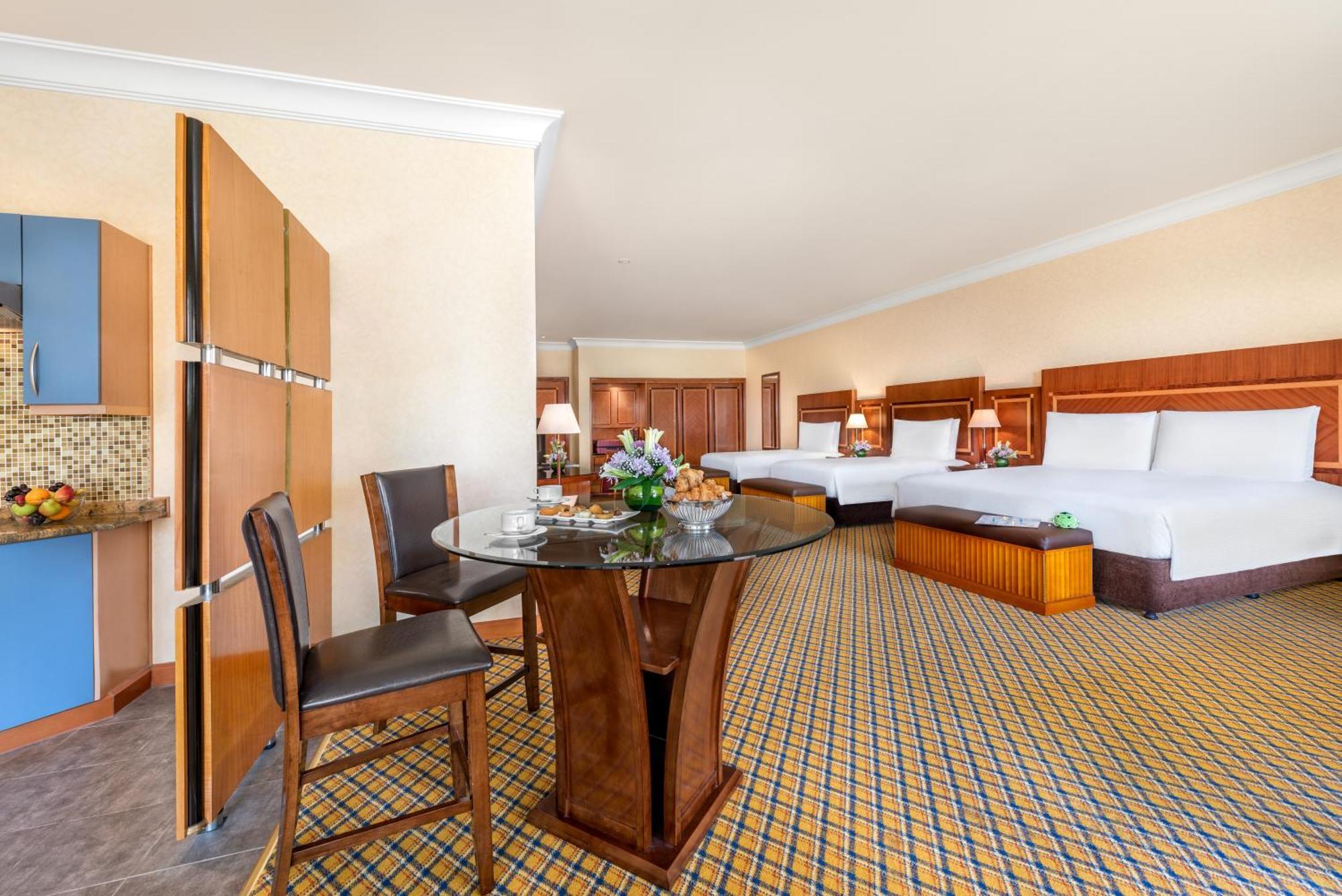 Al Raha Beach Resort & Spa Abu Dabi Habitación foto The photo displays a spacious hotel room. It features two large beds with white bedding, a circular glass dining table with a decorative floral centerpiece, and a couple of chairs around it. There is a wooden cabinet along one wall, and the room has 