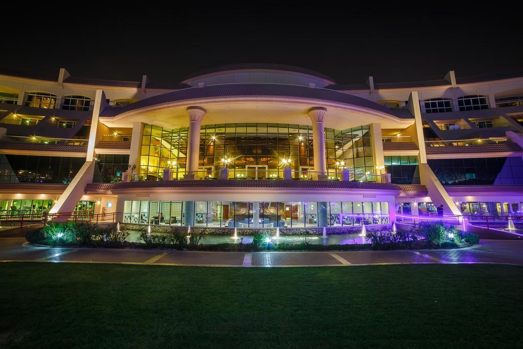 Al Raha Beach Resort & Spa Abu Dabi Exterior foto The photo shows a modern architectural building illuminated at night. The structure has a large central entrance with multiple glass windows, flanked by symmetrical columns. The exterior features a combination of sleek lines and curves, with lighting